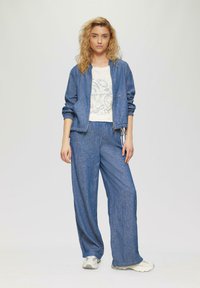 Denim jas en wijde broek in een blauwe stof. Witte T-shirt met een bedrukte afbeelding. Lichtgekleurde sneakers. Casuele sportieve outfit.