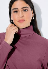 Langärmeliges Rollkragenoberteil aus weichem, strukturiertem mauvefarbenem Stoff. Verfügt über ein leicht tailliertes Design mit gerippten Details am Kragen und an den Bündchen.