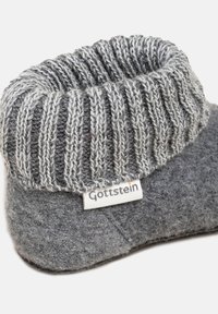 Pantofola di lana grigia con bordo a coste ripiegato, caratterizzata da un'etichetta bianca con il nome del marchio "Gottstein" cucita sul lato.