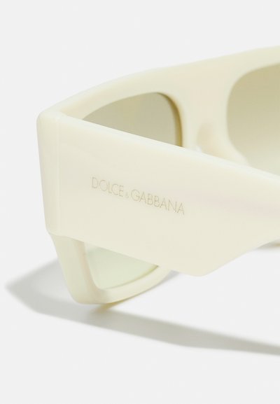 Ochelari de soare Dolce & Gabbana cu un cadru mat de fildeș, formă unghiulară și lentile verzi; au logo-ul gravat pe tâmple.
