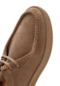 Zapato de ante marrón con punta redonda, detalles de costura a lo largo del borde y una textura suave. Presenta un diseño con cordones y suela flexible.