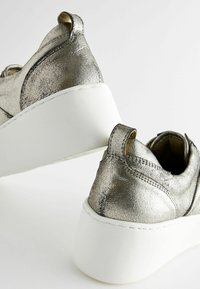 Metallic silver sneakers with a white platform sole; features a textured finish, rounded shape, and pull tab at the heel.