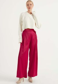 Witte cropped trui met een V-hals en losse mouwen, gecombineerd met hooggewaiste, wijde fuchsia broek en nude hakken.