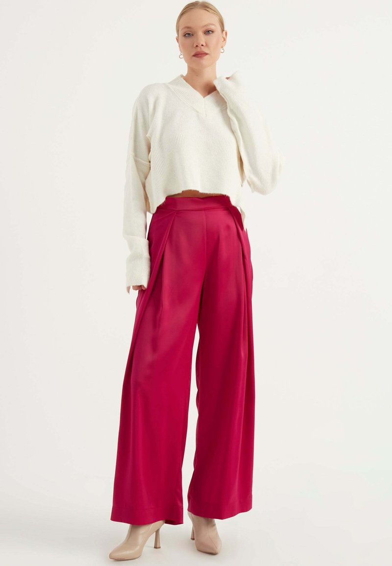 Witte cropped trui met een V-hals en losse mouwen, gecombineerd met hooggewaiste, wijde fuchsia broek en nude hakken.