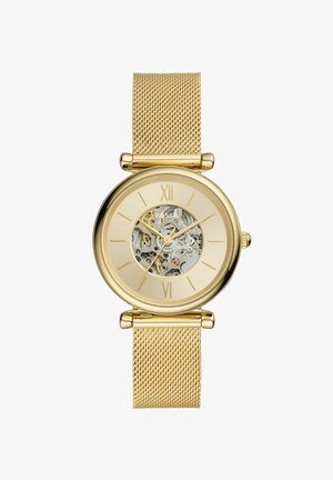 Orologio con cinturino in maglia metallica dorata, cassa rotonda, quadrante trasparente che mostra il movimento e numeri romani alle posizioni 12 e 6.