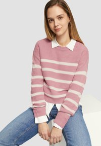 Rosa Strickpullover mit weißen Streifen, weitem Ausschnitt und gerippten Bündchen, über einem weißen Hemd getragen, kombiniert mit blauen Jeans.