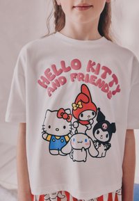 T-shirt en coton blanc avec un imprimé coloré de Hello Kitty et ses amis. Manches courtes, col rond, personnages de dessin animé aux designs variés.