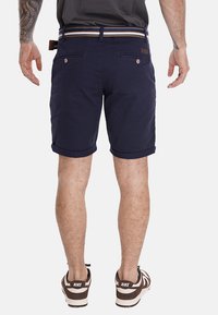 Pantaloni corti in cotone blu navy con risvolti, dotati di due tasche posteriori e una cintura a righe. I dettagli includono una patch in pelle con logo.
