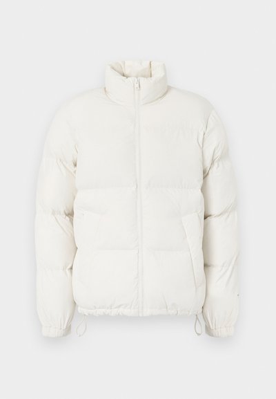 Krämfärgad pufferjacka med hög krage, framsidans blixtlås och elastiska ärmslut. Har slätt tyg och ett quiltat mönster med sidofickor.