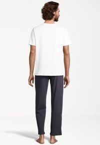 Weißes Baumwoll-T-Shirt und dunkelgraue Lounge-Hosen. Das T-Shirt hat einen runden Ausschnitt, und die Hose ist schmal geschnitten mit einer glatten Textur.