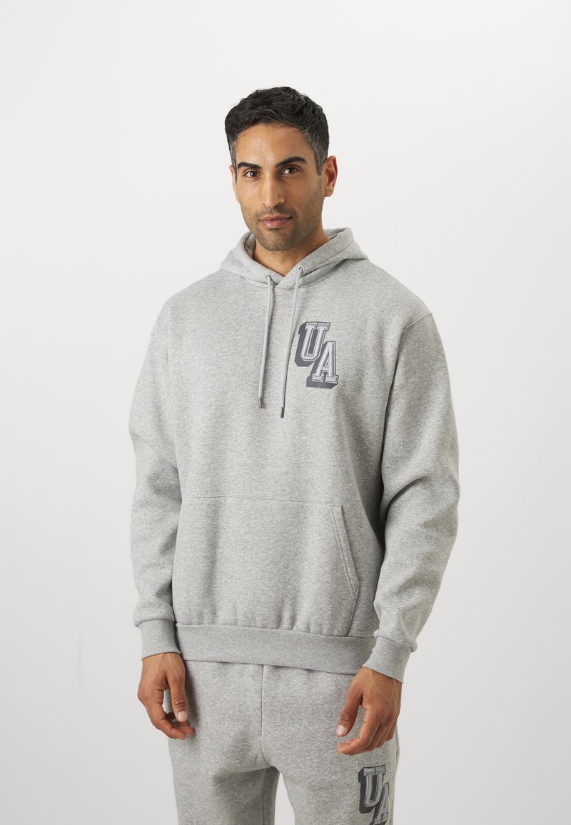 Sudadera gris hecha de un tejido suave, con un bolsillo frontal, capucha con cordón y logo "UA" en gris más oscuro en el pecho.