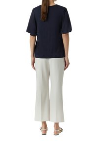 Marineblaues T-Shirt mit kurzen Ärmeln und rundem Ausschnitt, kombiniert mit weitem weißen Hosen. Das Model steht mit dem Rücken zur Kamera.