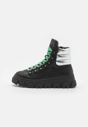 Baskets montantes en cuir noir avec un col rembourré argenté, des lacets verts, et une semelle en caoutchouc noir épaisse avec des rainures distinctes.