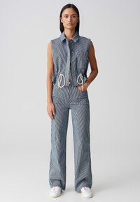 Veste en denim sans manches avec un motif rayé et une taille à cordon, assortie à un pantalon taille haute dans le même tissu et le même design.
