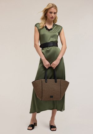 Vestido de satén verde oliva con mangas cortas, cinturón ancho negro y un gran bolso de mimbre con asas y detalles negros. Sandalias deslizables negras.