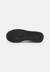 Talpa de sneaker din cauciuc negru, cu un model texturat pentru aderență și un logo circular. Include margini ridicate și caneluri pentru tracțiune.