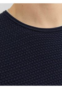 Tume sinine tekstuuriga sviiter kudumise mustriga, millel on ümmargune ribakrae ja pehme kangas. Suumvaade krae alale.