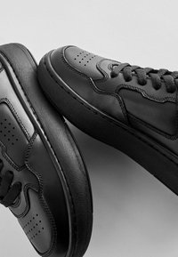 Svarta lädersneakers med rundad tå, perforerade detaljer, texturerad gummisula och platta skosnören i en klassisk design.