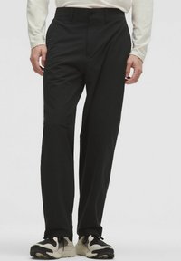 Pantaloni neri a gamba dritta in tessuto tessuto, con chiusura frontale a bottone e tasche laterali. Abbinati a sneakers nere e bianche.