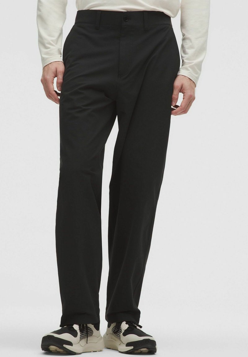 Pantaloni neri a gamba dritta in tessuto tessuto, con chiusura frontale a bottone e tasche laterali. Abbinati a sneakers nere e bianche.