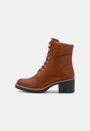 Brown leather ankle boot with a rounded toe, gold eyelets, laces, and a chunky black heel. Smooth texture with a classic design.