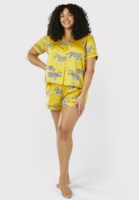 Gule satin pajamas med sorte zebra mønstre, med korte ærmer og shorts, designet med knaplukning og røde detaljer.