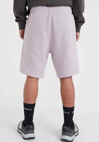 Bermudas de sudadera lavanda claro con cintura elástica, bolsillos laterales y un corte holgado. Combinadas con medias negras hasta la rodilla y zapatillas.