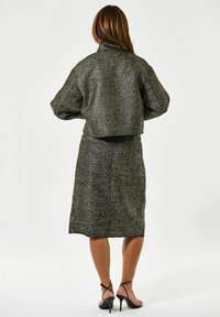 Juoda ir metalizuota pilka medžiaga, trumpa struktūrinė striukė ir pieštuko sijonas; turi raktinius pečius ir elegantišką dizainą.