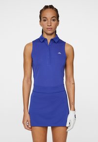 Ärmlös blå polo-klänning med krage, figurnära midja och slät yta. Har en liten vit logotyp på bröstet och en vit handske.