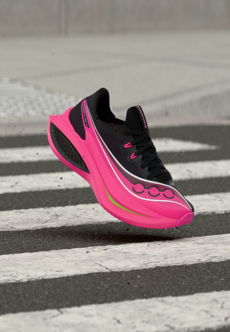 Μαύρο και φωτεινό ροζ αθλητικό παπούτσι με χοντρή σόλα, στον αέρα πάνω από μια διάβαση πεζών σε ασφάλτινο δρόμο.