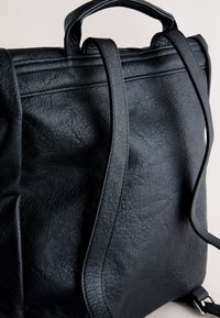 Sac à dos en cuir noir avec bretelles réglables et une poignée supérieure, montrant un matériau texturé et des coutures détaillées.