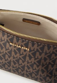 Smeđa platnena torbica s zlatnim patentnim zatvaračem, ukrašena uzorkom "MK" logotipa po cijeloj površini i s oznakom Michael Kors unutra.