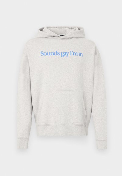 Svijetlosiva majica s kapuljačom i prednjim džepom, s plavim natpisom "Sounds gay I'm in" u sredini prsa.