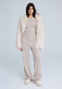 Completo a due pezzi a coste beige con pantaloni a gamba larga e top aderente, indossato sotto un morbido cappotto di pelliccia sintetica crema, abbinato a scarpe chiare.