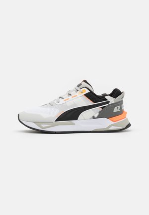 Białe, szare i czarne sportowe buty z pomarańczowymi akcentami, siatkowanym noskiem, grubą podeszwą i czarnym logo Puma z boku, przedstawione z widoku bocznego.