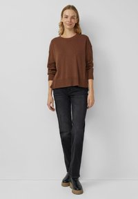 Brązowy dzianinowy sweter z prążkowanym dołem, w połączeniu z ciemnymi dżinsami i czarnymi botkami. Model charakteryzuje się luźnym krojem i okrągłym dekoltem.
