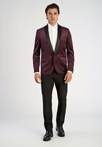 Mörk röd sammetsfrack med svarta satinrevers, kombinerad med vit skjorta och svarta byxor, med två framfickor och eleganta skor.