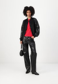Čierna umelá kožená bomber bunda, červený top, čierne široké nohavice z umelej kože a čižmy na opätku. Malá čierna kabelka ako detail.