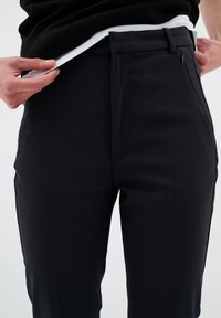 Black tailored pants feature a smooth texture, slim fit, and side pockets. Waistband includes a subtle belt loop.