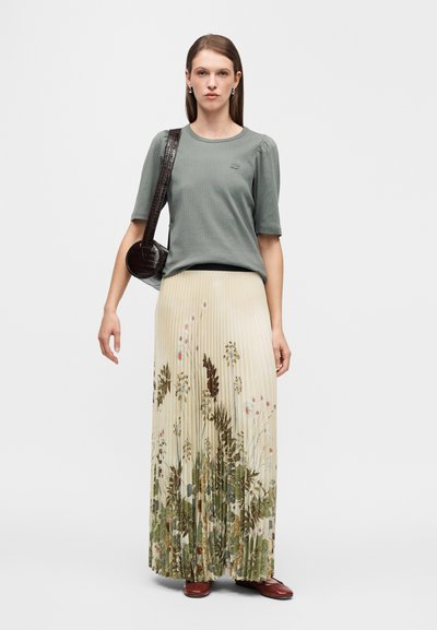 Γκρι ριμπ κοντομάνικη μπλούζα σε συνδυασμό με μακριά πλισέ φούστα με λουλουδάτο σχέδιο σε απαλούς τόνους του πράσινου, μπεζ και ροζ, συμπληρωμένη με κόκκινα παπούτσια.