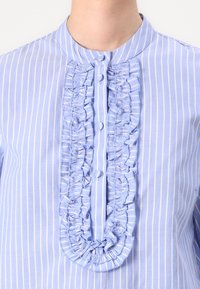 Chemise rayée bleu clair avec un col rond, un détail froncé à l'avant et des boutons le long de la patte. Fabriquée en tissu léger.