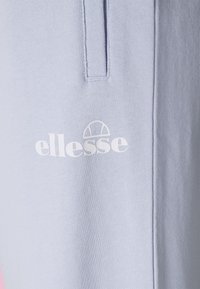 Světle modrá mikinová látka s texturovaným povrchem; obsahuje bílé logo "ellesse" a vertikální šev jako designový prvek.