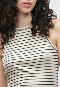 Prążkowany top na ramiączkach wykonany z rozciągliwej tkaniny, z cienkimi czarnymi paskami na jasnobeżowym tle, z wysokim dekoltem i bez rękawów.