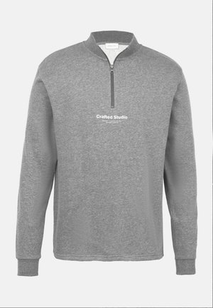 Sudadera gris con cremallera y mangas largas, hecha de un material suave, que presenta un cuello alto y el texto "Crafted Studio" en la parte delantera.