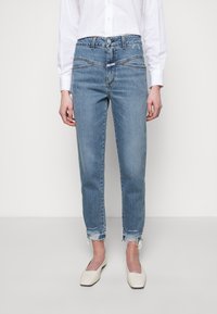 Jean en denim bleu clair à taille haute, coupe droite, ourlets déchirés et poches avant. Associé à des ballerines blanches à bout pointu.