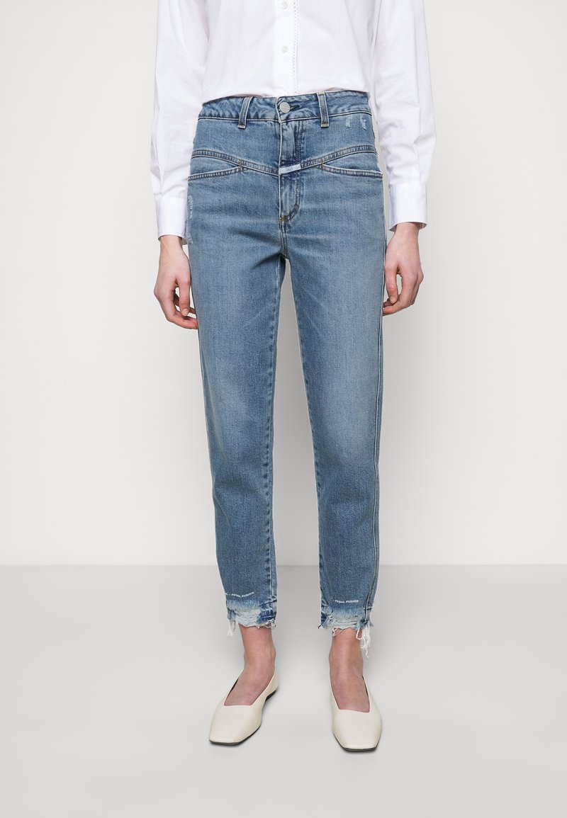 Jean en denim bleu clair à taille haute, coupe droite, ourlets déchirés et poches avant. Associé à des ballerines blanches à bout pointu.