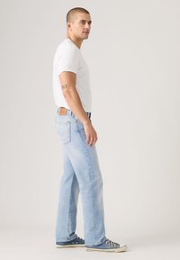 Šviesiai mėlynos spalvos džinsai iš džinso audinio, laisvo silueto, su tiesiais kojų pjūviais, išblukusia tekstūra ir rudos odos išsiuvinėta dėmė gale ant juostos.