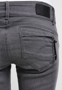 Grå denimjeans med en ficka med dragkedja, förstärkt sömnad och en läderlogotyp på midjan. Slim fit-design.
