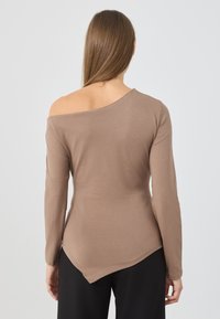 Brun, tettsittende langermet topp med asymmetrisk halslinje, myk tekstur og en midje-lang hemline, kombinert med svarte bukser.