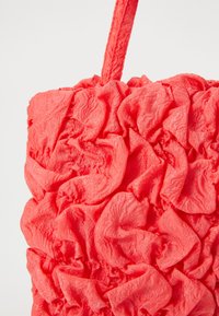 Borsa a mano con texture corallo e design arricciato. Il materiale è morbido e leggermente lucido, con un motivo di tessuto intricato e stratificato.